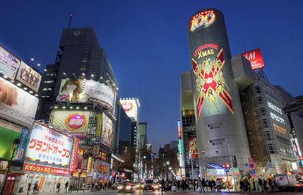 A vibrant night view of a busy Tokyo street corner with large, illuminated buildings and advertisements.