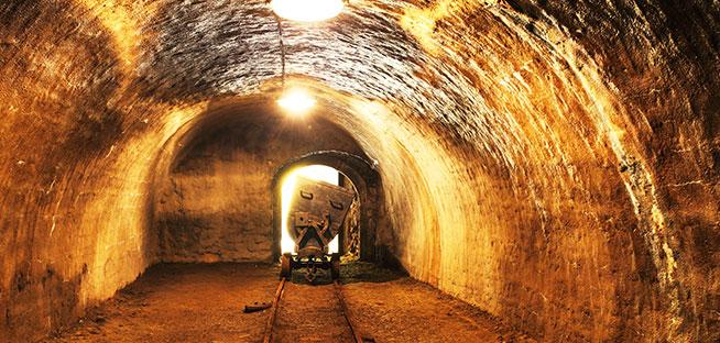 Interior of a dark, low-lit mine tunnel with a cart on tracks.