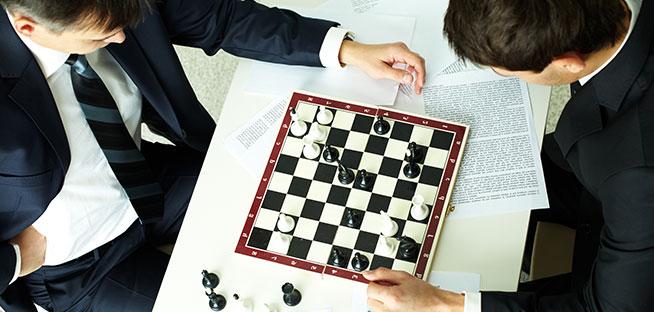 Overhead view of two individuals in business suits engaged in a game of chess on a table.