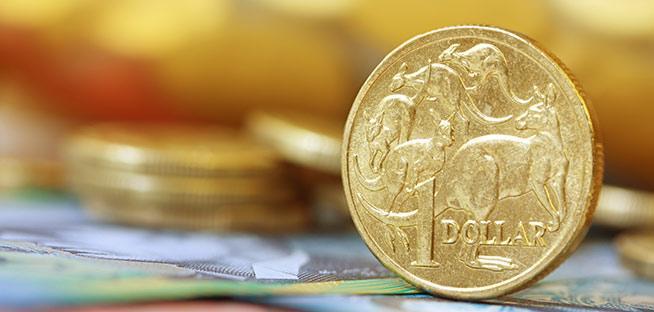 Close-up of an Australian one-dollar coin, showing the kangaroo design, resting on a banknote with more coins blurred in the background.