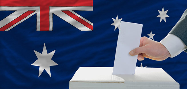 Hand casting a vote into a ballot box with the Australian flag in the background.