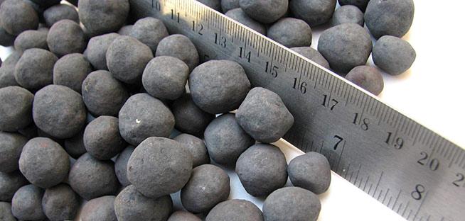 Metal ruler measuring the size of dark, round iron ore pellets.
