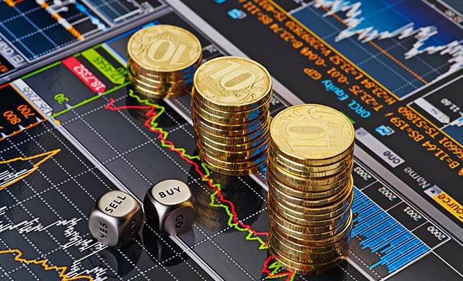 Stacks of gold coins and dice labeled "BUY" and "SELL" sit on top of financial charts.