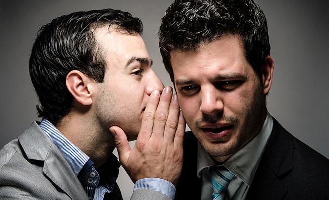 Man whispering a secret or rumor into another man's ear.