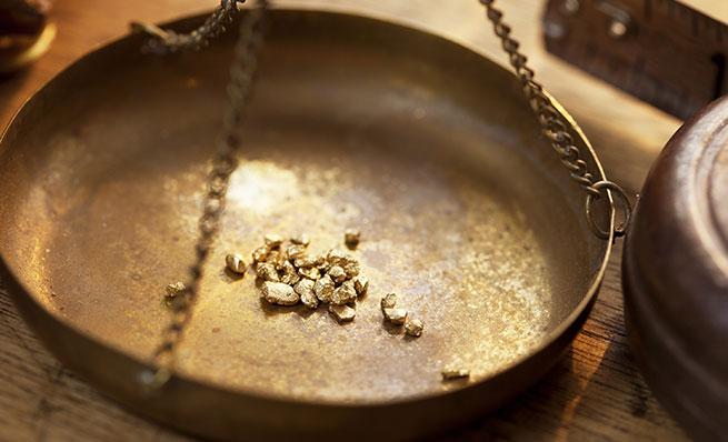 Small gold nuggets in the brass pan of an old weighing scale.