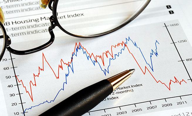Pen and reading glasses on a chart showing two volatile, opposing stock lines.