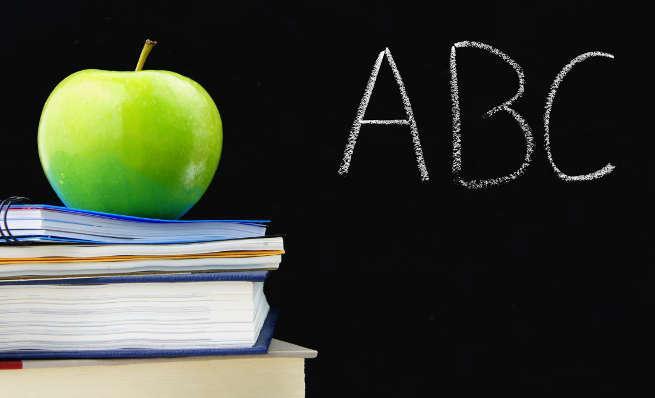 Green apple on a stack of books next to 'ABC' written on a chalkboard.