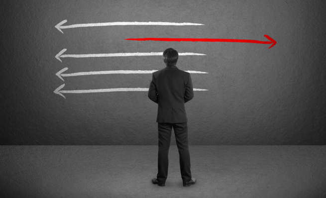 Businessman facing a wall with arrows, with one red arrow pointing the opposite way.