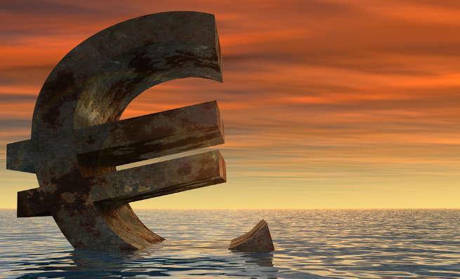 Large Euro symbol sinking in the sea at sunset.