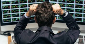 Stressed trader clenching hair while looking at multiple monitors of stock market charts.
