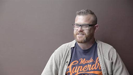Bearded man named David H with short gray hair and glasses, smiling in a gray cardigan.
