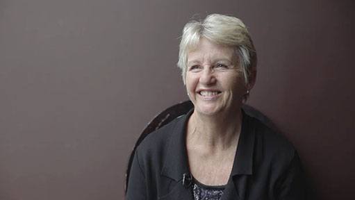 An older woman named Jeannie K with short gray hair smiling warmly in a dark jacket.