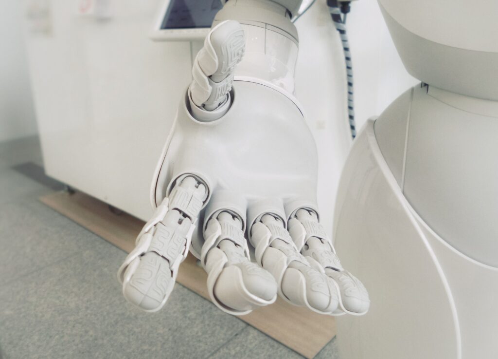 A close-up, high-key photo of a white, articulated robotic hand extended toward the viewer, possibly symbolizing artificial intelligence (AI) or future technology.