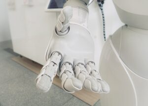 A close-up, high-key photo of a white, articulated robotic hand extended toward the viewer, possibly symbolizing artificial intelligence (AI) or future technology.