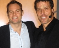 A photo of two men, one resembling Tony Robbins with a headset microphone, posing with their arms around each other and smiling for a picture.