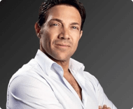 A portrait of a man with dark hair and blue eyes, wearing an unbuttoned white collared shirt, against a solid dark gray-green background.